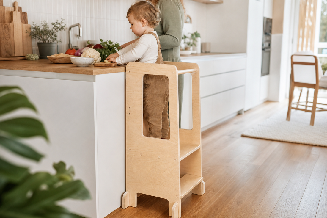 Toddler standing safely in a wooden Montessori learning tower at a kitchen counter