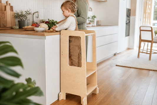 Toddler standing safely in a wooden Montessori learning tower at a kitchen counter
